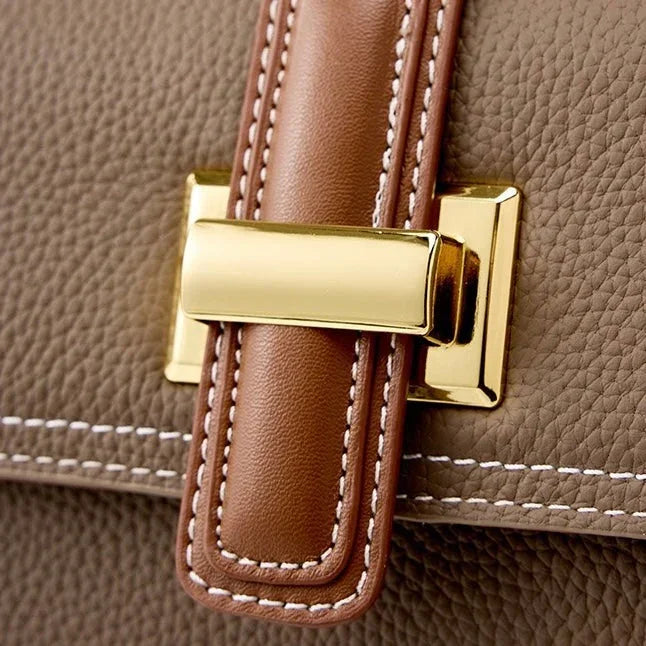 Close-up of brown leather handbag with gold clasp and white stitching