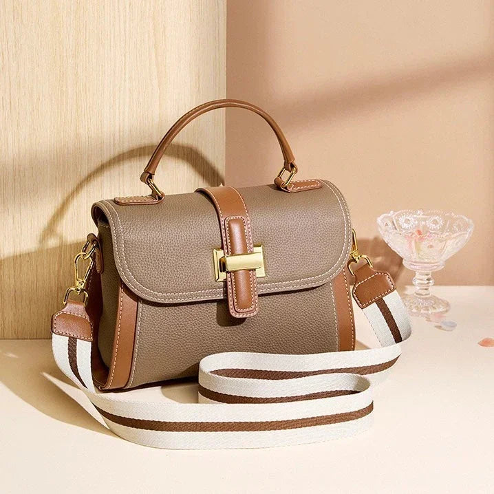 Taupe leather handbag with brown accents and gold hardware on beige surface, striped strap