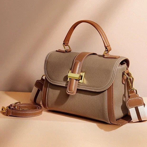 Taupe leather handbag with brown trim, gold clasp, and detachable strap on beige background