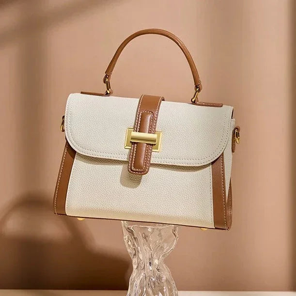 Beige and brown leather handbag with top handle and gold buckle against neutral background