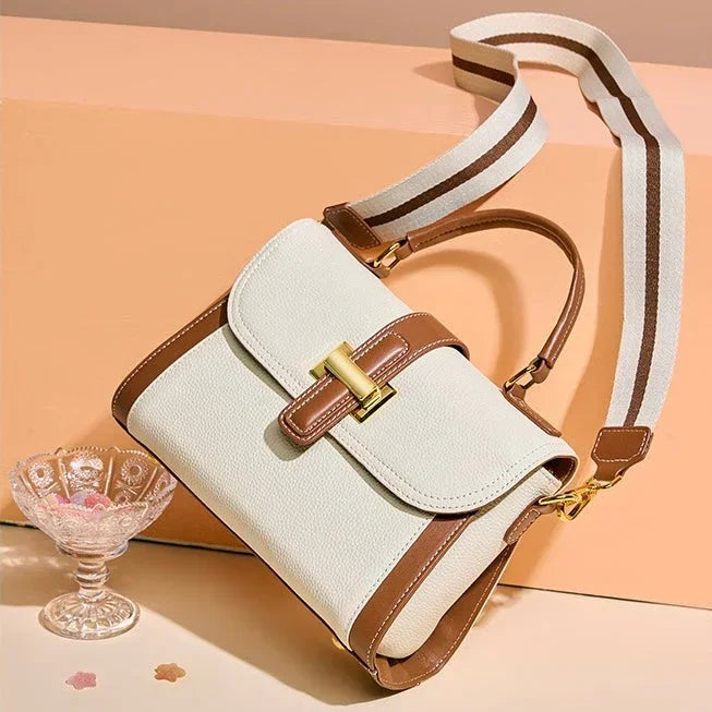 White and brown leather crossbody handbag with gold clasp on peach background