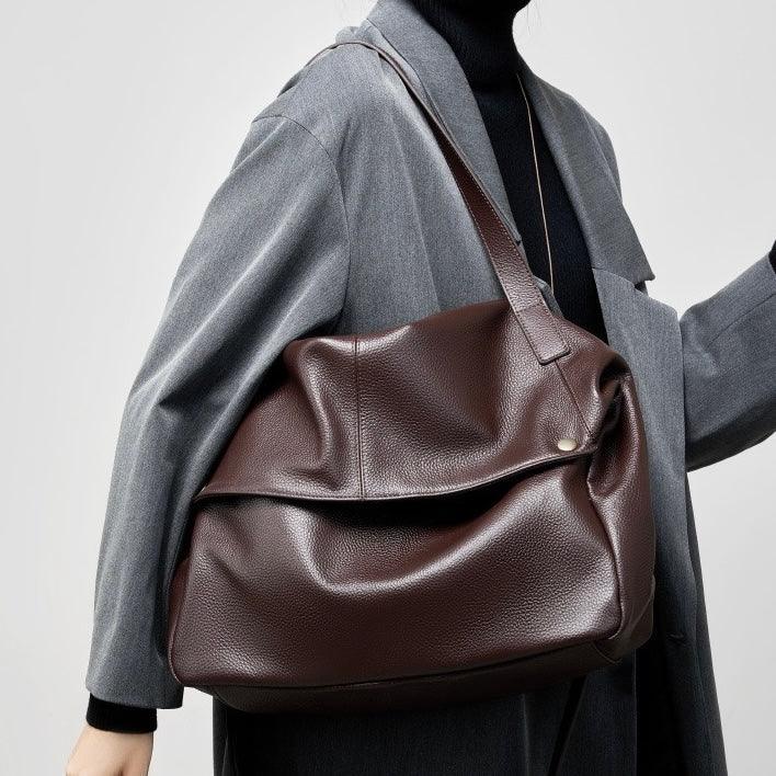 Woman in gray coat carrying large brown leather tote bag over shoulder