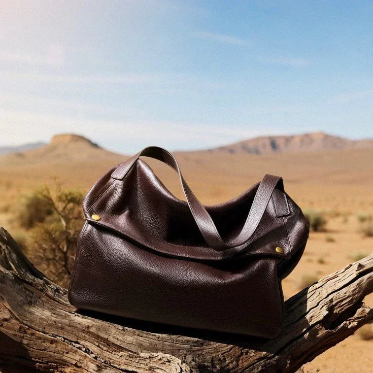 Brown leather tote bag on a tree branch in a desert landscape with mountains