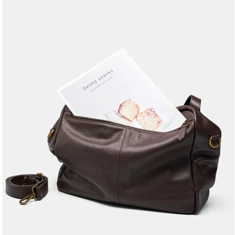 Dark brown leather duffel bag with detachable strap and magazine on white background