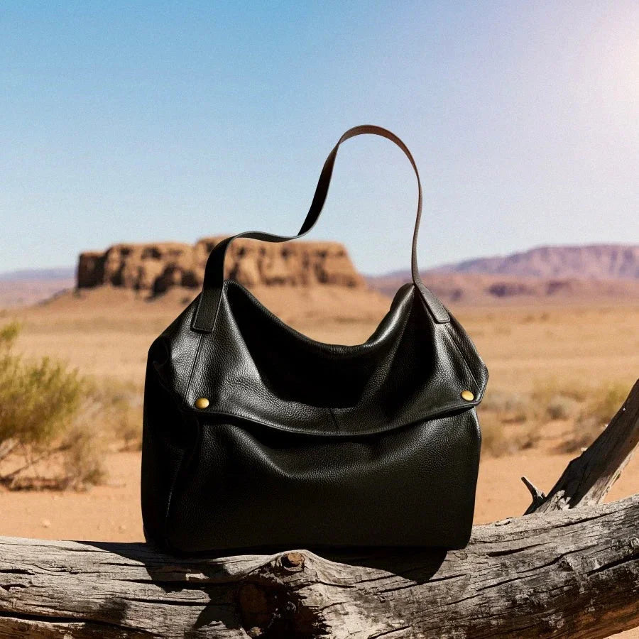 Black leather shoulder bag on a log in a desert landscape with rocky mesas.