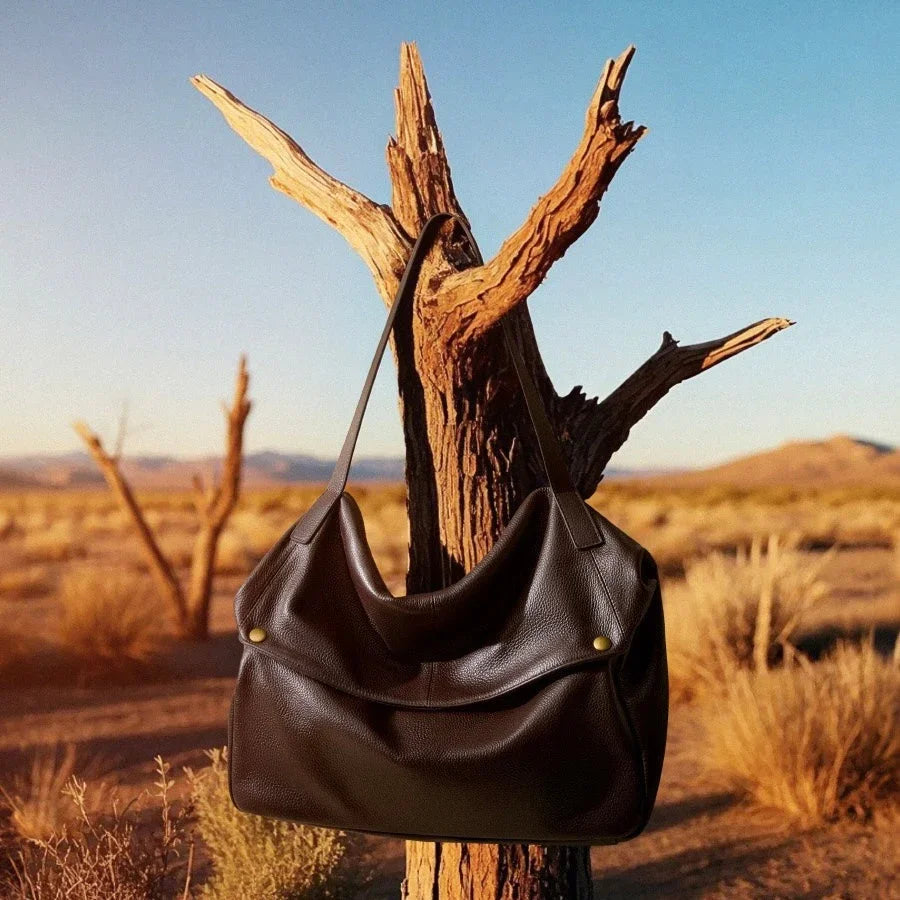 Black leather shoulder bag hanging on a tree in a desert landscape