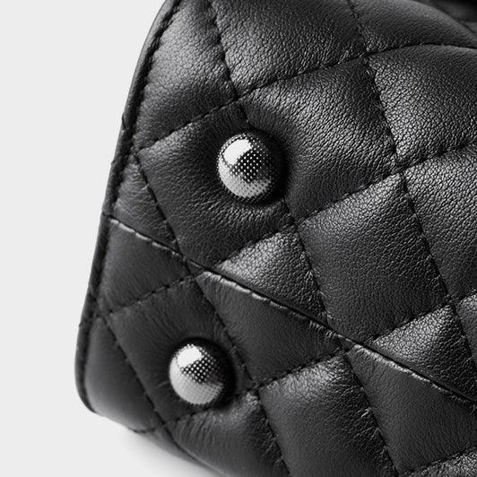 Close-up of quilted black leather bag with silver stud details on a light background