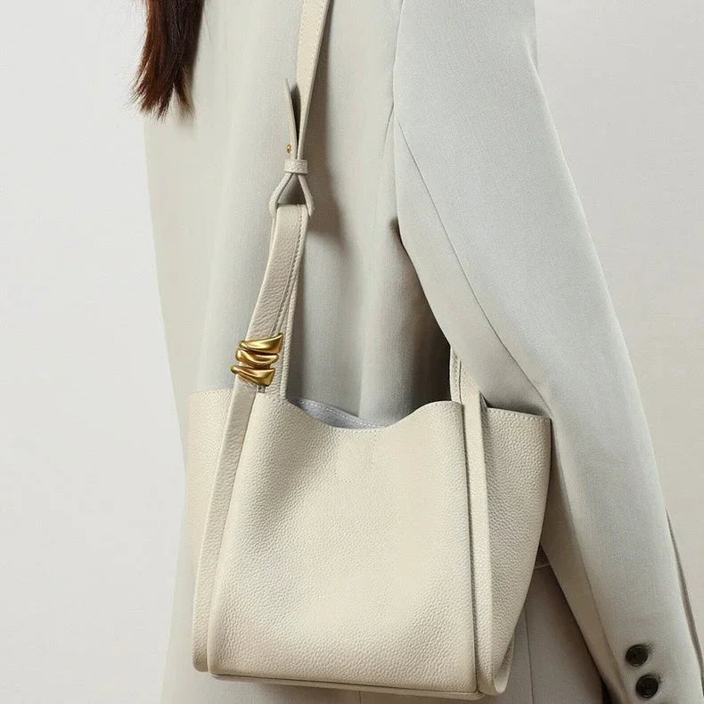 Woman in light blazer carrying a cream leather shoulder bag with gold accent detail
