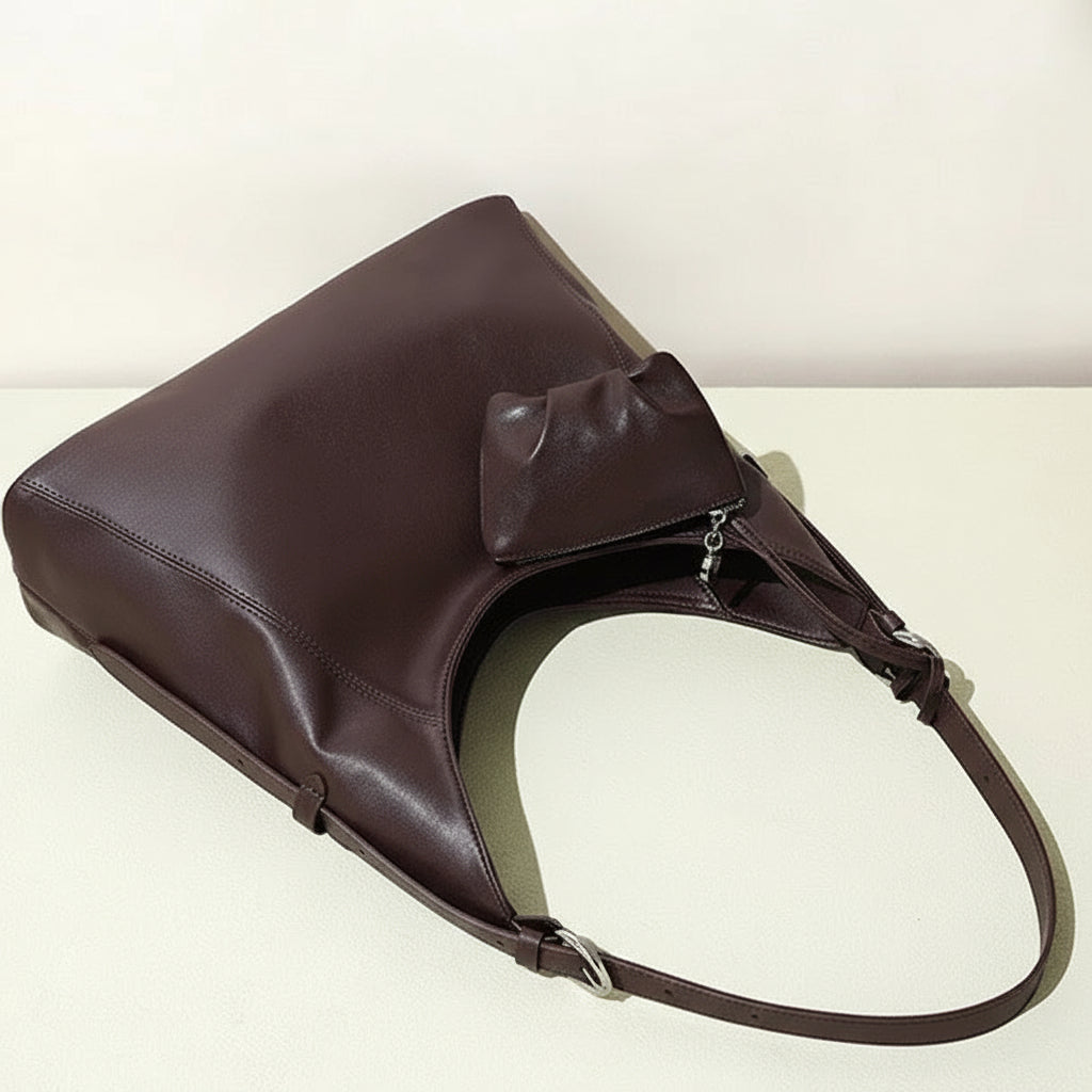 Brown leather tote bag with long strap and attached pouch on a light surface