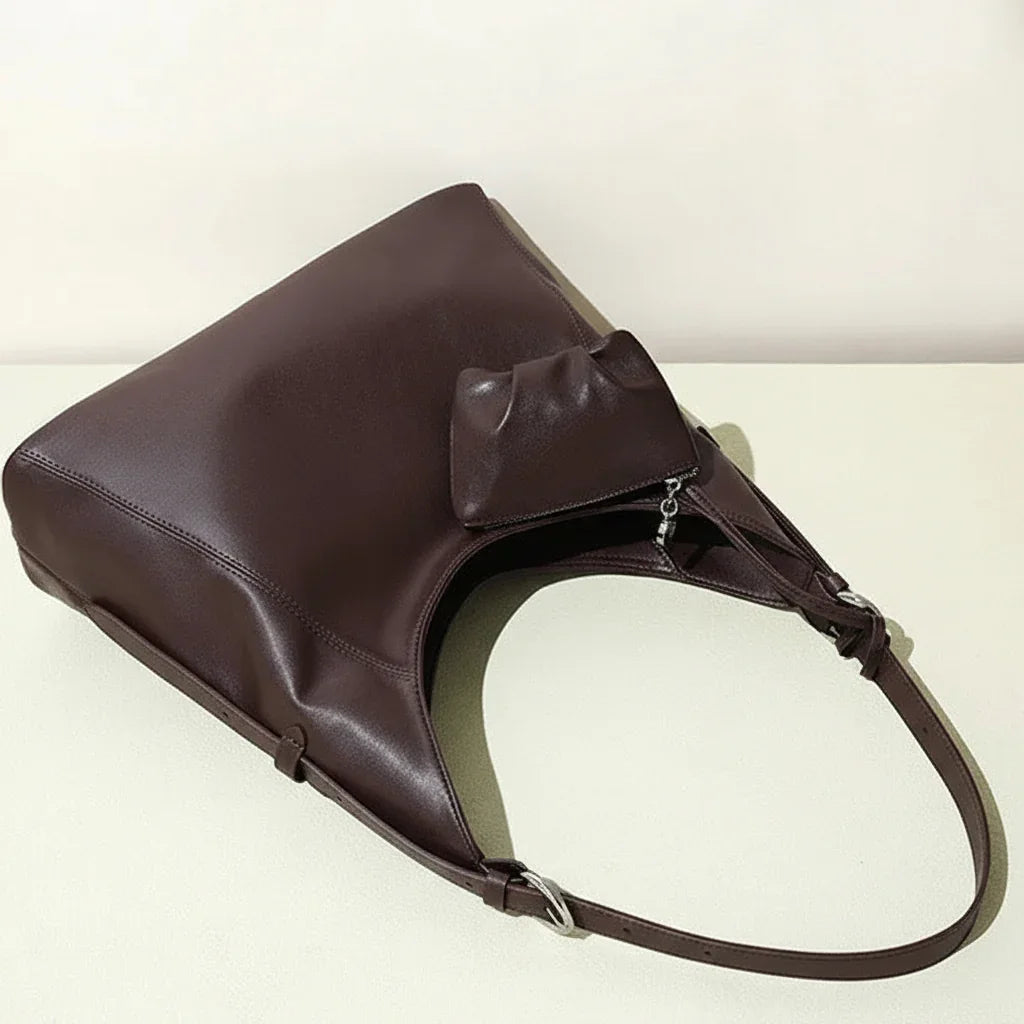 Brown leather tote bag with long strap and attached pouch on a light surface