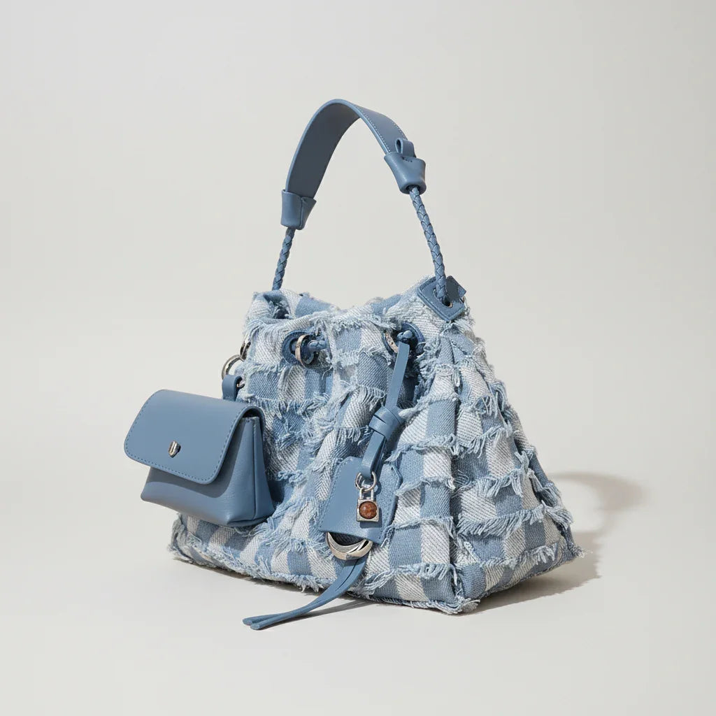 Blue plaid denim handbag with braided handle and attached mini pouch on beige background