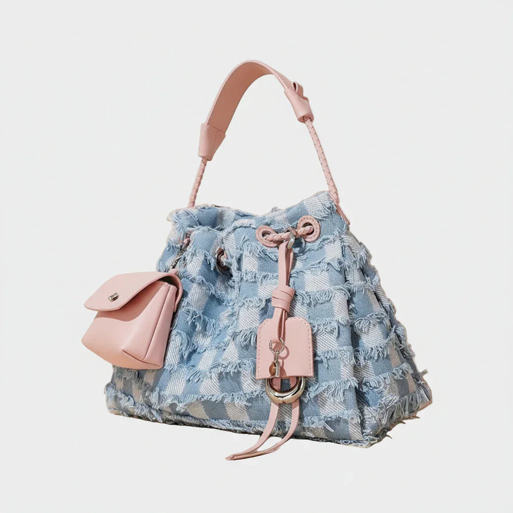Chic blue denim bucket bag with pink leather handle and accents on beige background