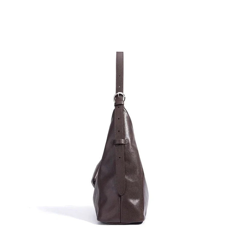 Side view of a brown leather handbag with adjustable strap on white background