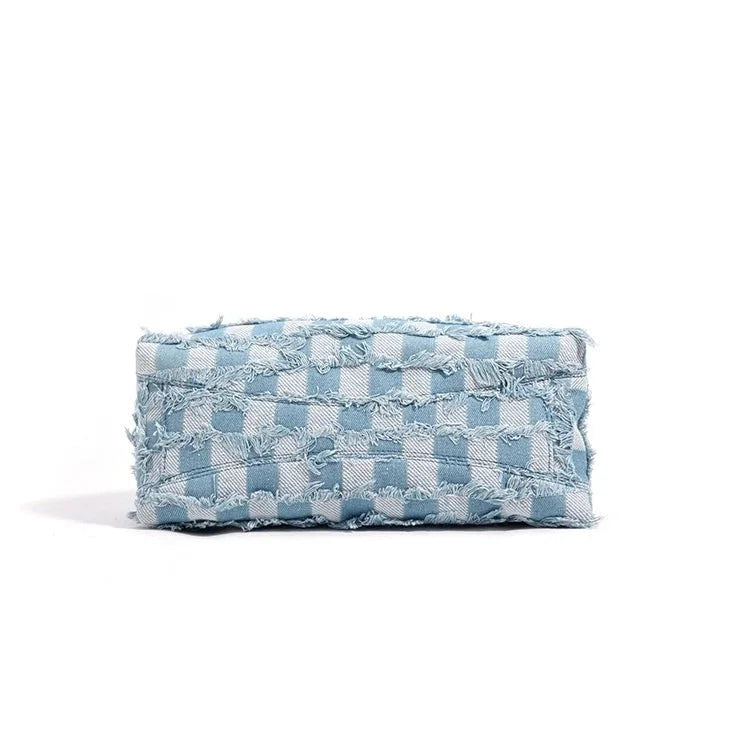 Light blue checkered denim clutch bag with frayed edges on white background