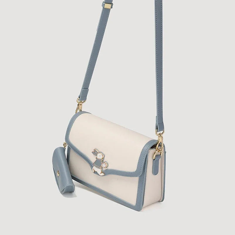Cream and blue crossbody bag with bunny accent and matching pouch on gray background
