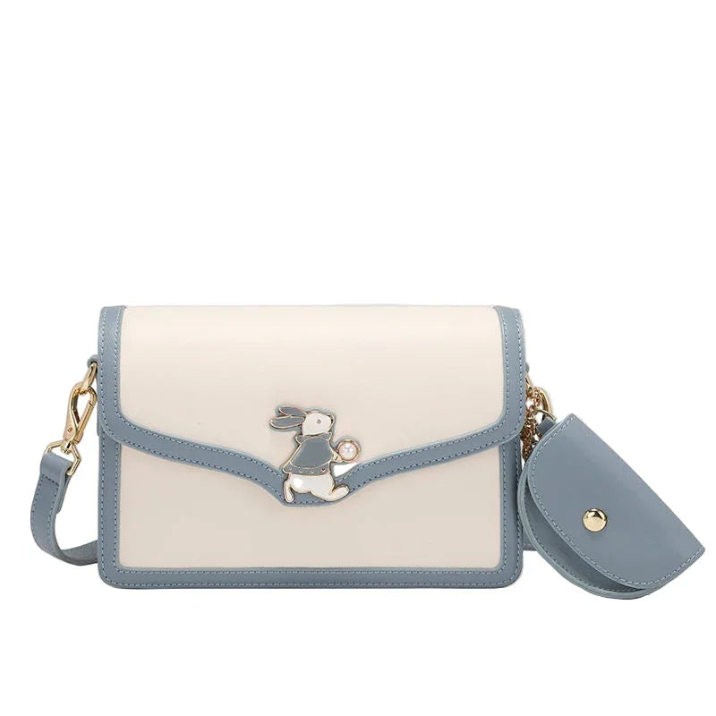 Blue and white crossbody bag with bunny charm and gold hardware on white background