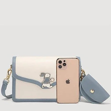 White and blue crossbody bag with bunny design, next to gold iPhone and matching pouch