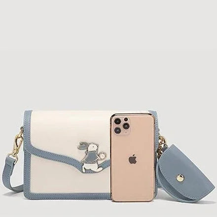 White and blue crossbody bag with bunny design, next to gold iPhone and matching pouch