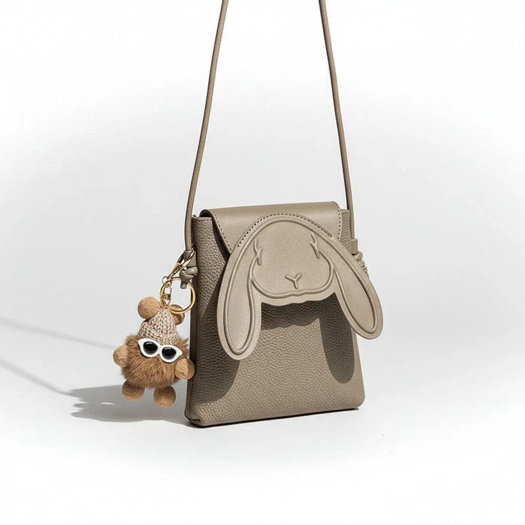 Beige crossbody bag with bunny ear design and teddy bear keychain with sunglasses