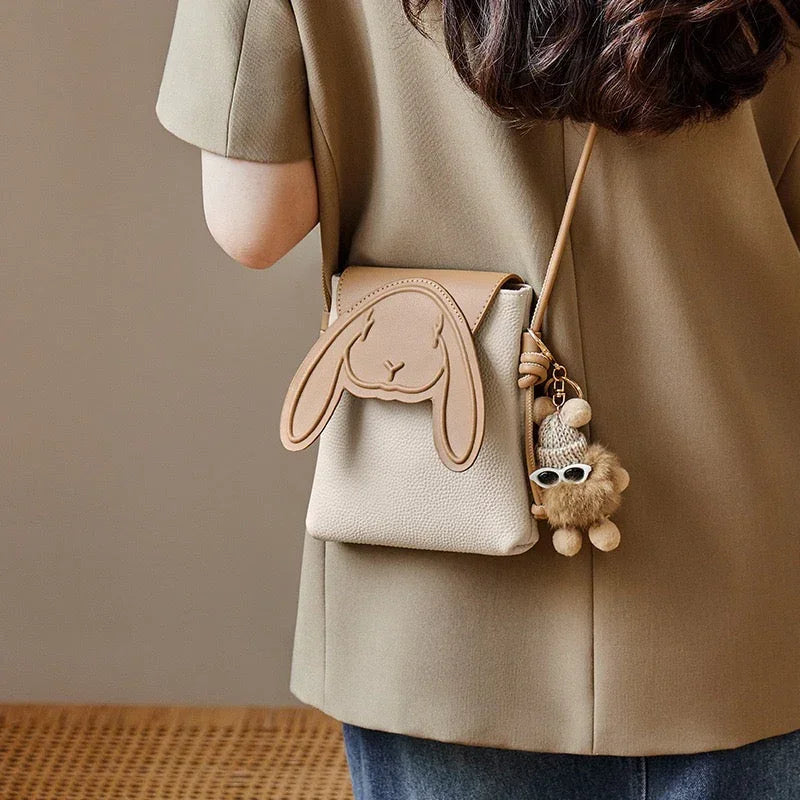 Woman wearing beige bunny ear crossbody bag with cute plush keychain accessory