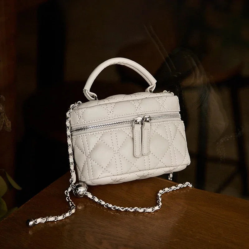 White quilted leather mini handbag with chain strap and zipper, on wooden table