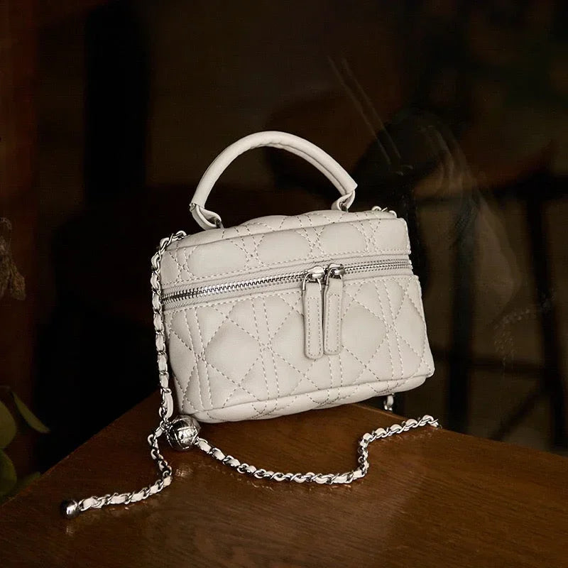 White quilted leather mini handbag with chain strap and zipper, on wooden table