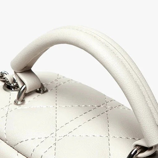 Close-up of white quilted leather handbag handle with silver hardware on a light background