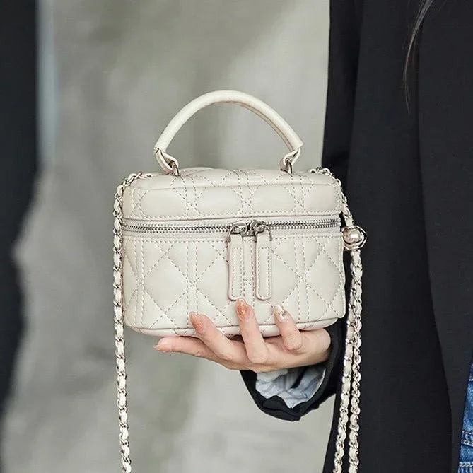 Elegant quilted beige mini handbag with top handle and chain strap, held by a woman