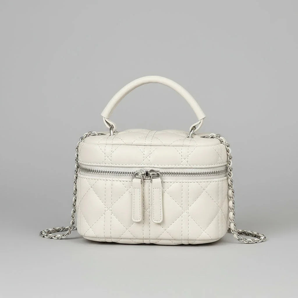 Quilted white leather handbag with top handle, silver chain strap, and front zipper on gray background