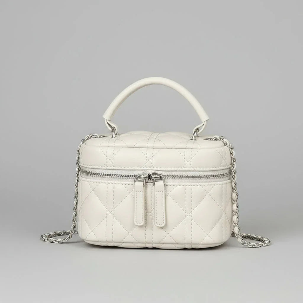 Quilted white leather handbag with top handle, silver chain strap, and front zipper on gray background