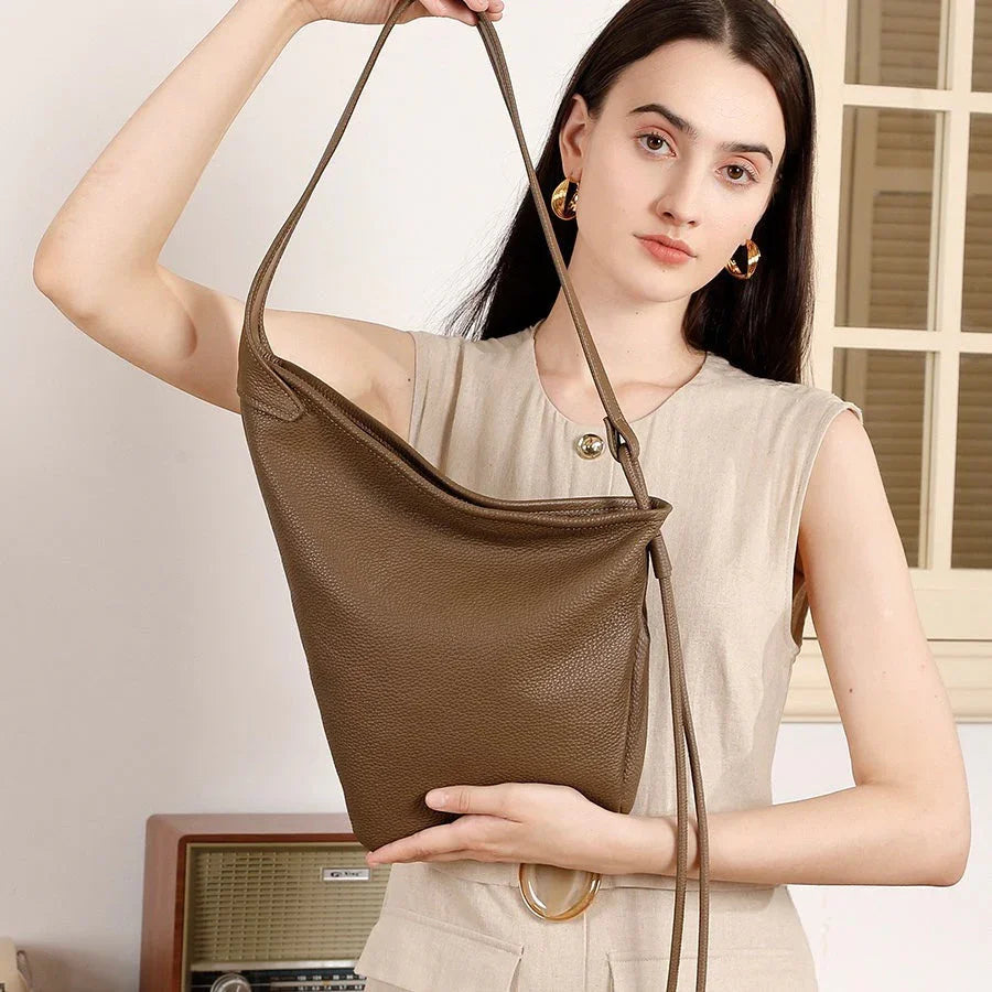 Woman holding large brown leather shoulder bag in minimalist indoor setting