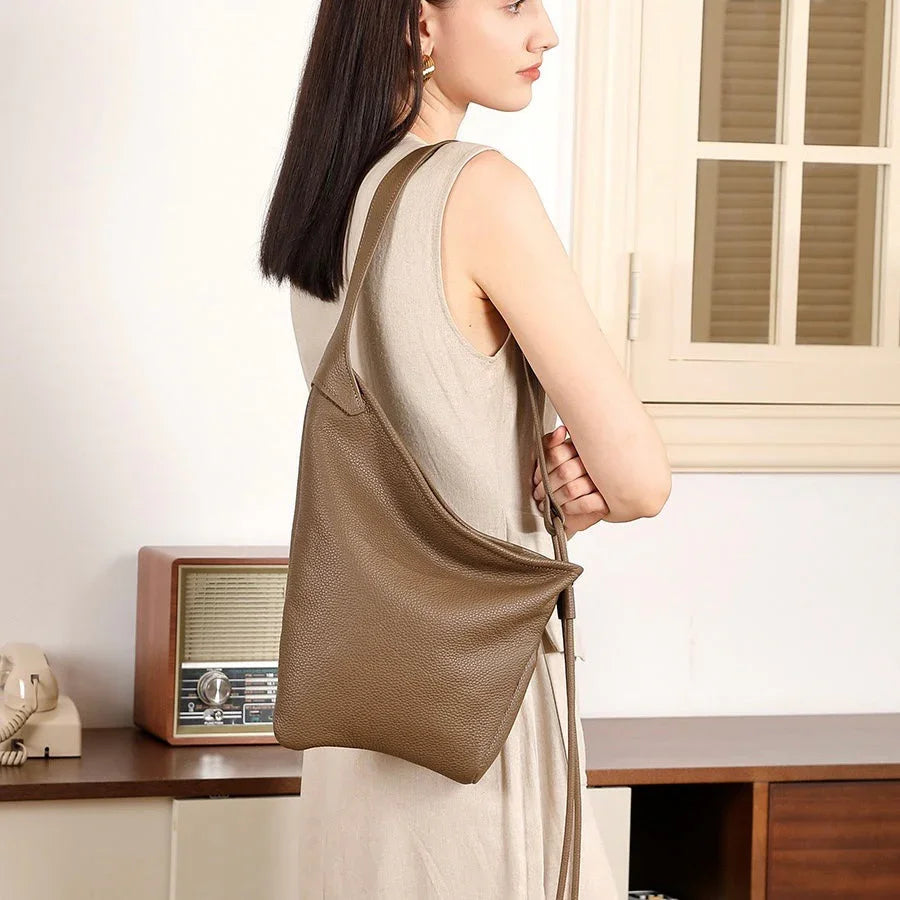 Woman wearing a minimalist brown leather shoulder bag in a modern interior setting