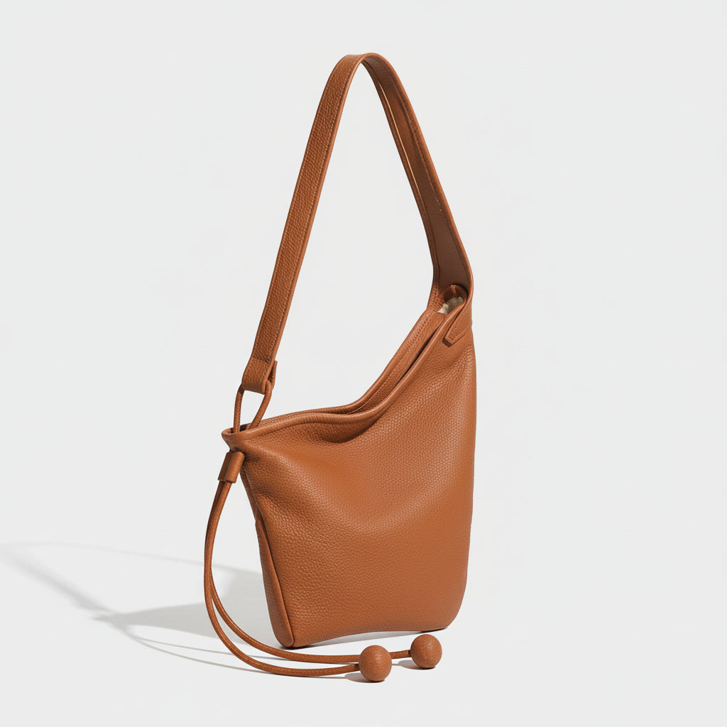 Brown leather shoulder bag with adjustable strap and ball tassel accents on white background.