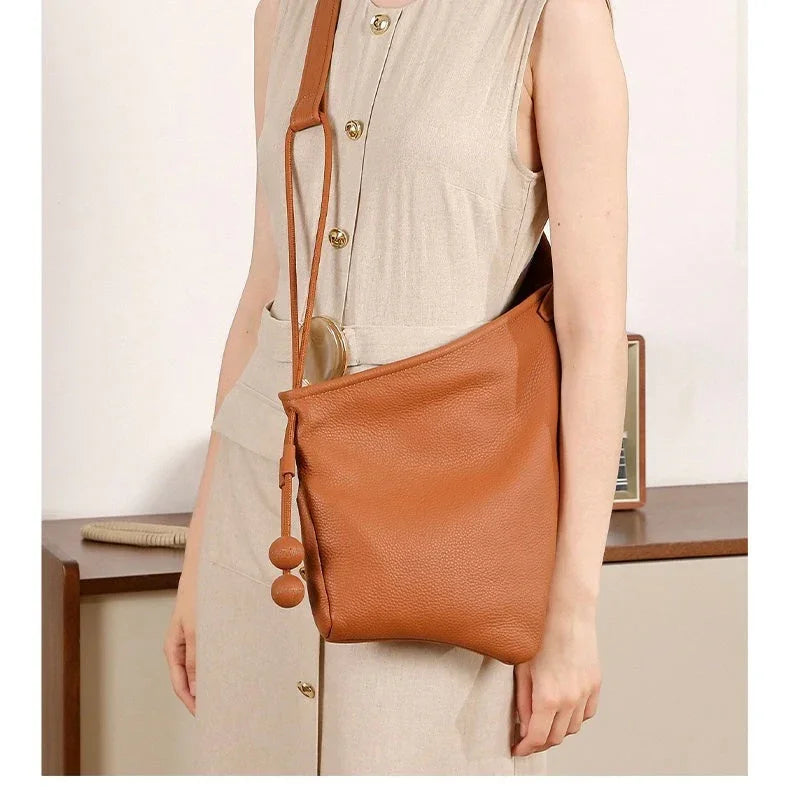 Woman in beige dress carrying a brown leather shoulder bag with decorative tassels