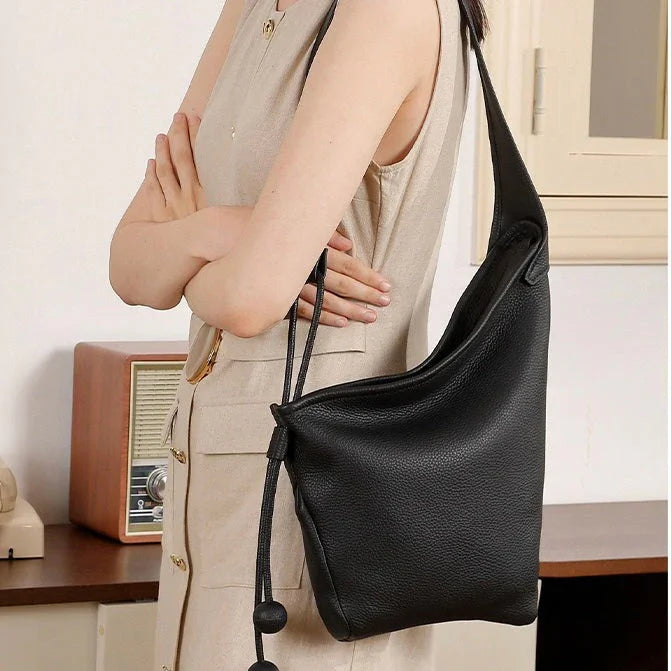 Woman wearing sleeveless beige dress with large black leather shoulder bag indoors