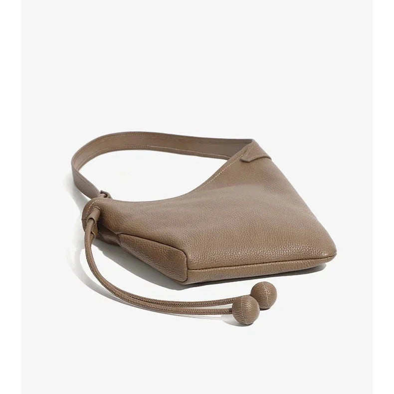 Taupe leather shoulder bag with a textured finish and drawstring detail on white background