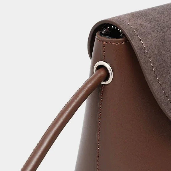 Close-up of brown leather handbag with silver grommet and stitching detail
