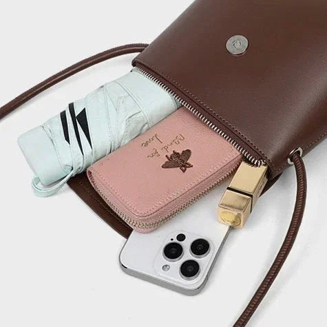 Brown crossbody purse with a folded umbrella, pink wallet, gold lipstick, and smartphone
