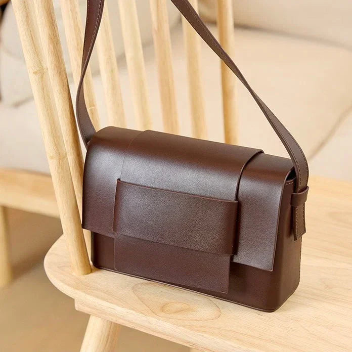Brown leather shoulder bag on wooden chair, minimalist design, crossbody purse