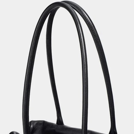 Close-up black leather handbag handles against a white background
