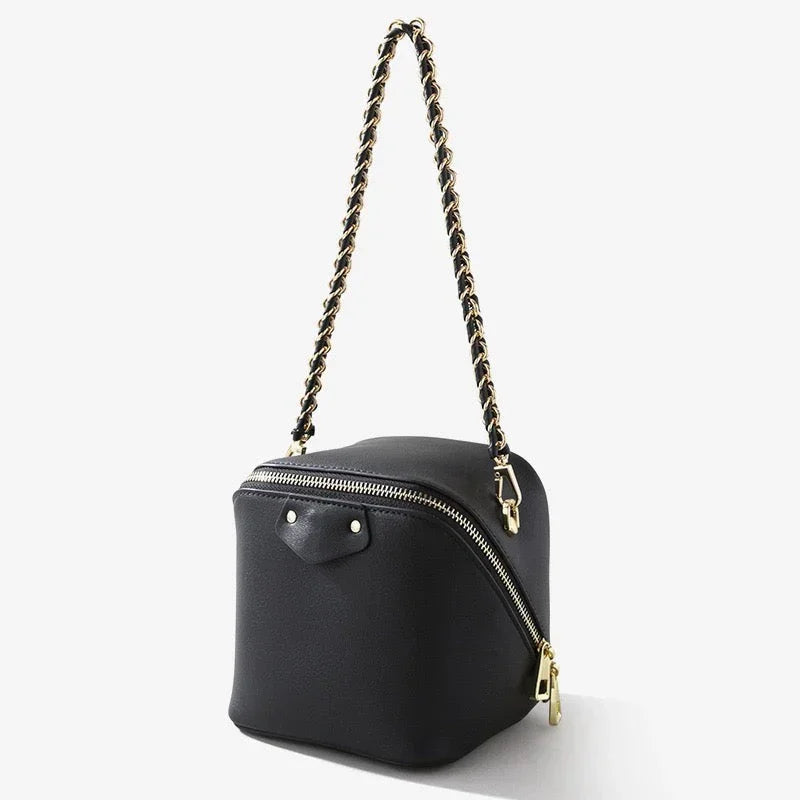Black leather box-shaped handbag with gold chain strap and zipper on white background