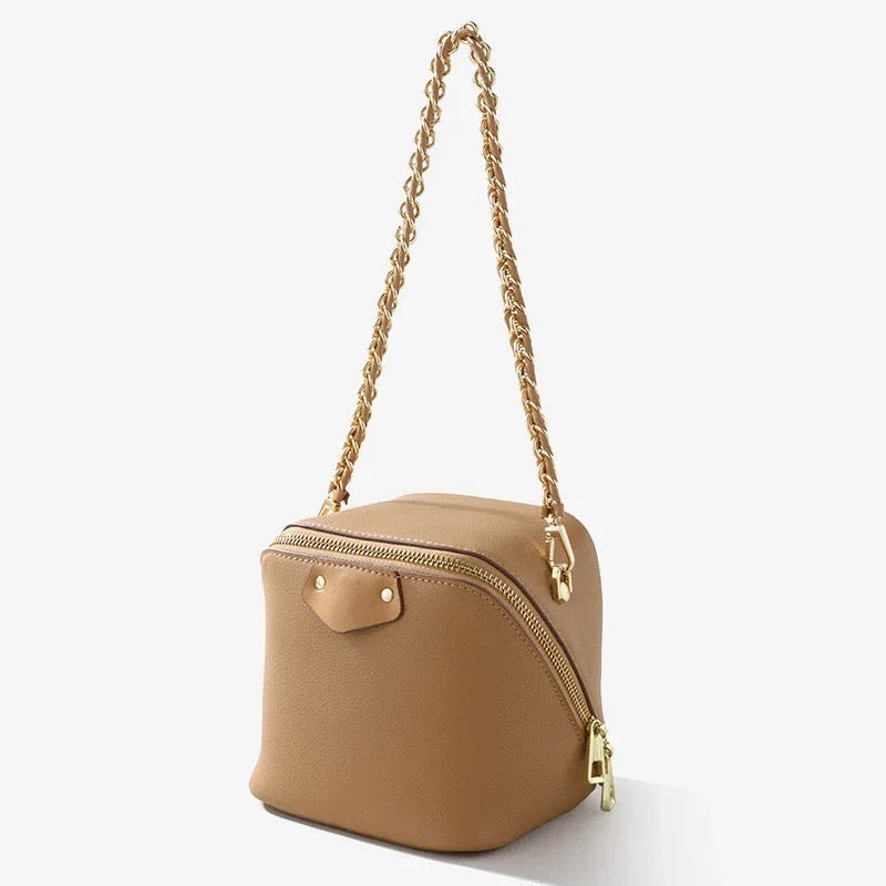 Tan leather box-shaped handbag with gold chain strap and zipper on white background