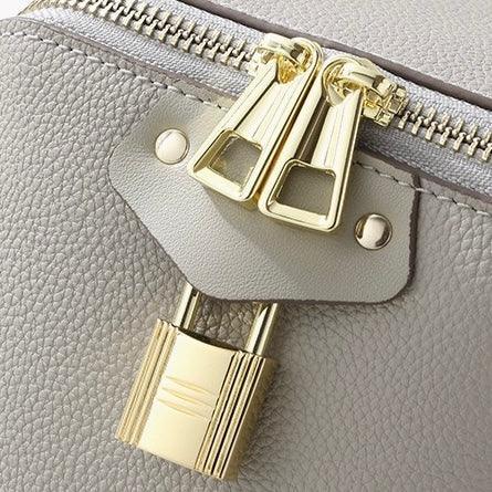 Close-up of a grey leather bag with gold zippers and a gold padlock detail