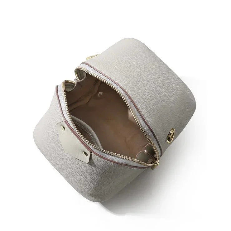Top view of an open gray leather cosmetic bag with gold zipper and beige lining