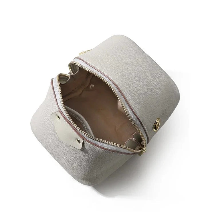 Top view of an open gray leather cosmetic bag with gold zipper and beige lining
