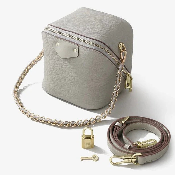 Gray leather crossbody bag with gold chain strap, extra strap, padlock, and key on white background