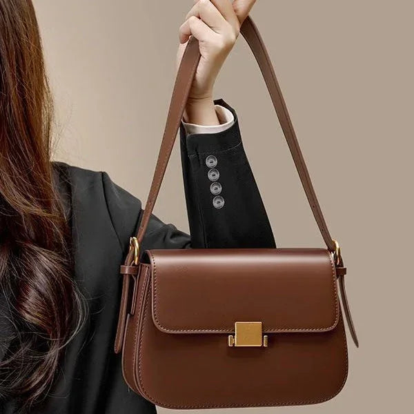 Woman in black blazer holding a brown leather shoulder bag with gold clasp