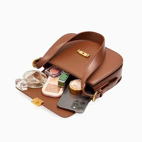 Brown leather crossbody bag open with cosmetics, perfume, and smartphone inside on white background