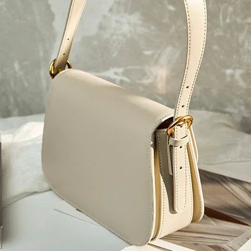 Beige leather shoulder bag with gold buckle details on a marble surface