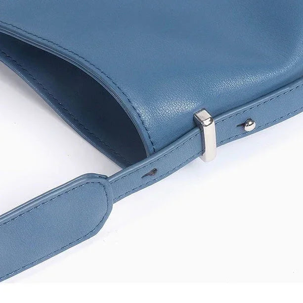 Blue leather shoulder bag with adjustable strap and silver buckle on white background